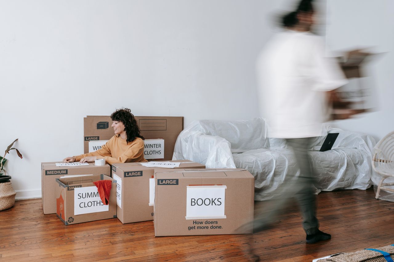 our-mission Un couple prépare le jour du déménagement en rangeant des cartons étiquetés dans un salon au style minimaliste.